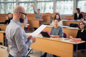Male professor reading from document in front of classroom