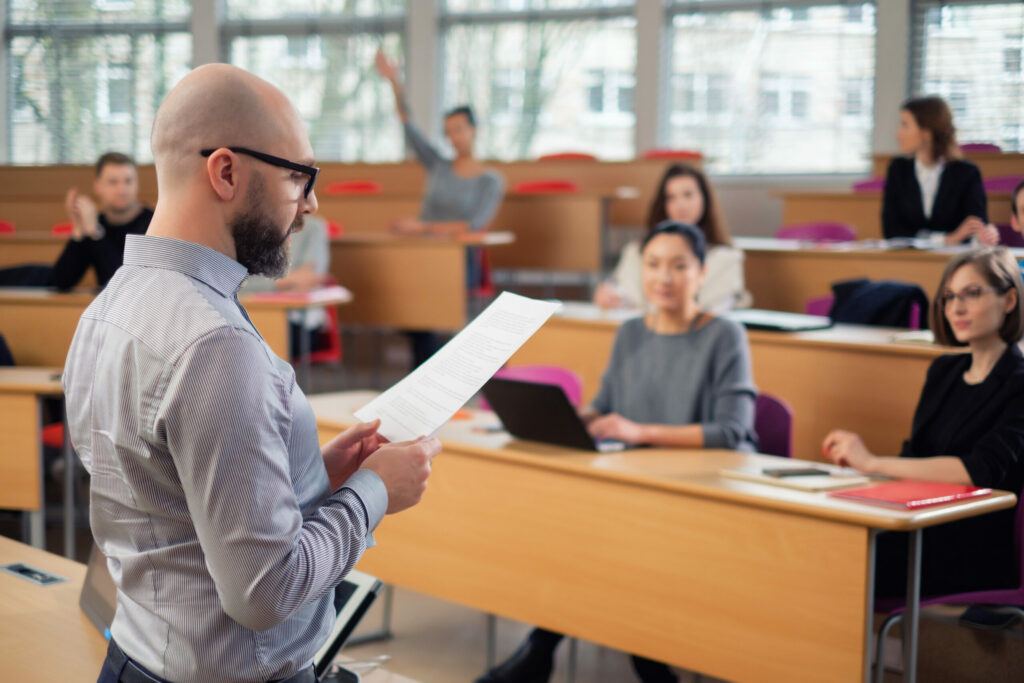 Male professor reading from document in front of classroom