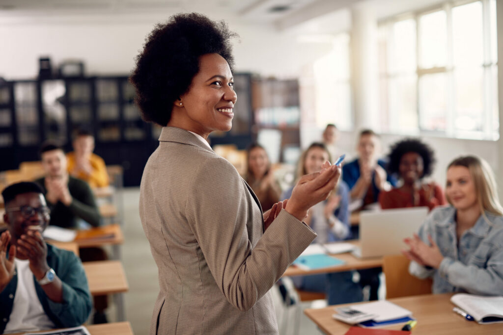 Female professor gesturing to board in front of college class